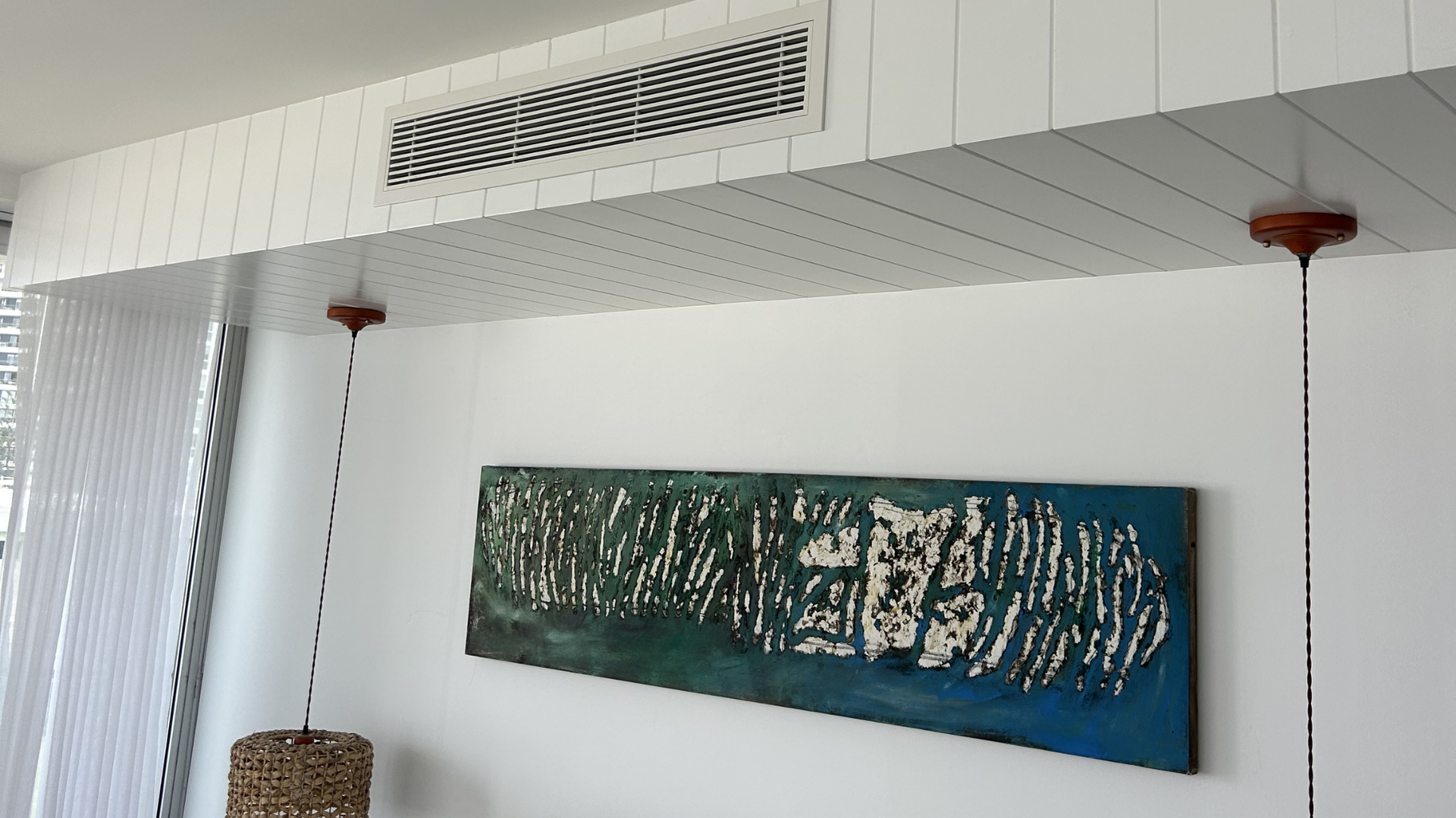 A white ceiling soffit with an AC vent and two hanging pendant lights over a textured blue and white abstract painting. — BTM Electrical & Air in Palm Beach, QLD