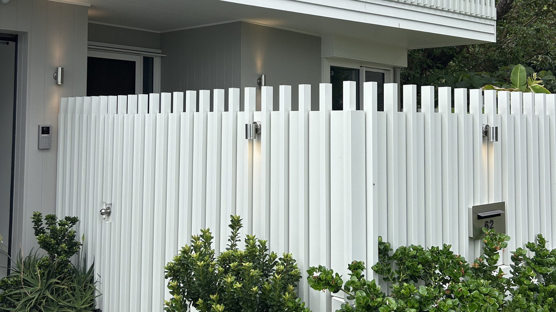 A white modern fence made of vertical metal slats features integrated wall-mounted lights in front of a house. — BTM Electrical & Air in Southport, QLD