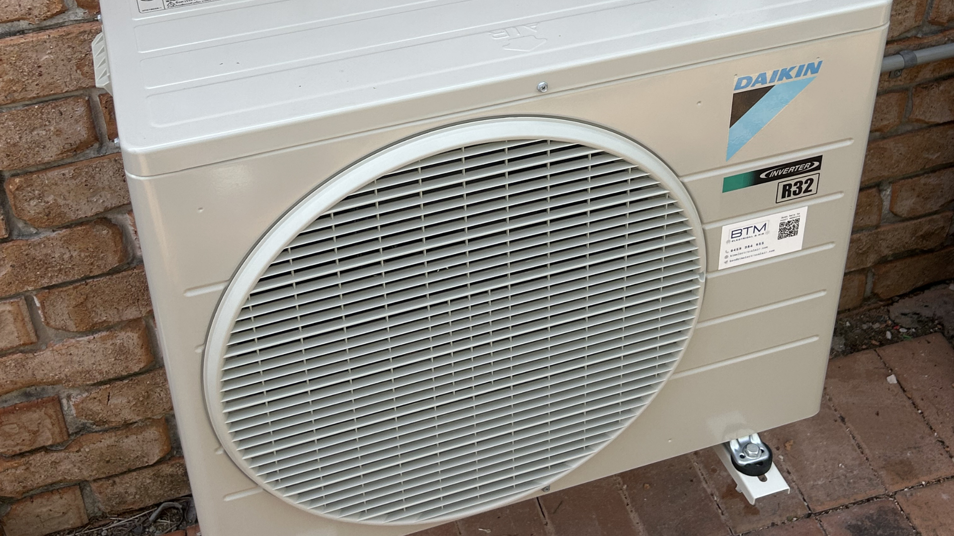 A beige Daikin outdoor air conditioning unit sits against a brick wall on a paved surface. — BTM Electrical & Air in Currumbin, QLD