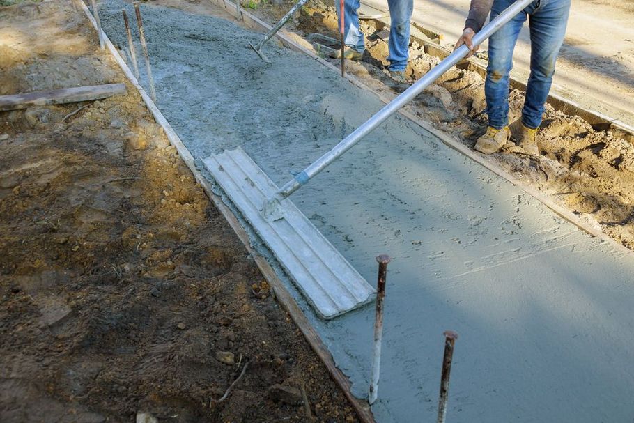 Construction worker using a bull float to smooth wet concrete for a sidewalk.
