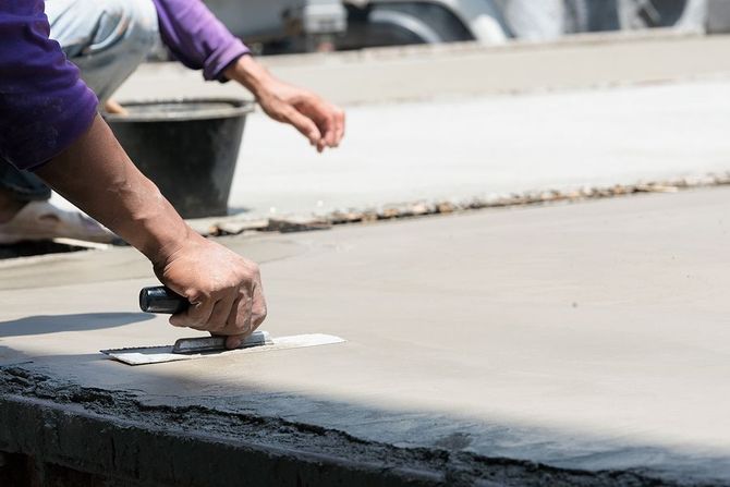 Worker smoothing wet concrete with a hand trowel.