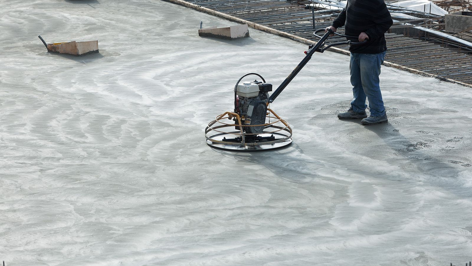 Construction worker operating a power trowel to smooth wet concrete.