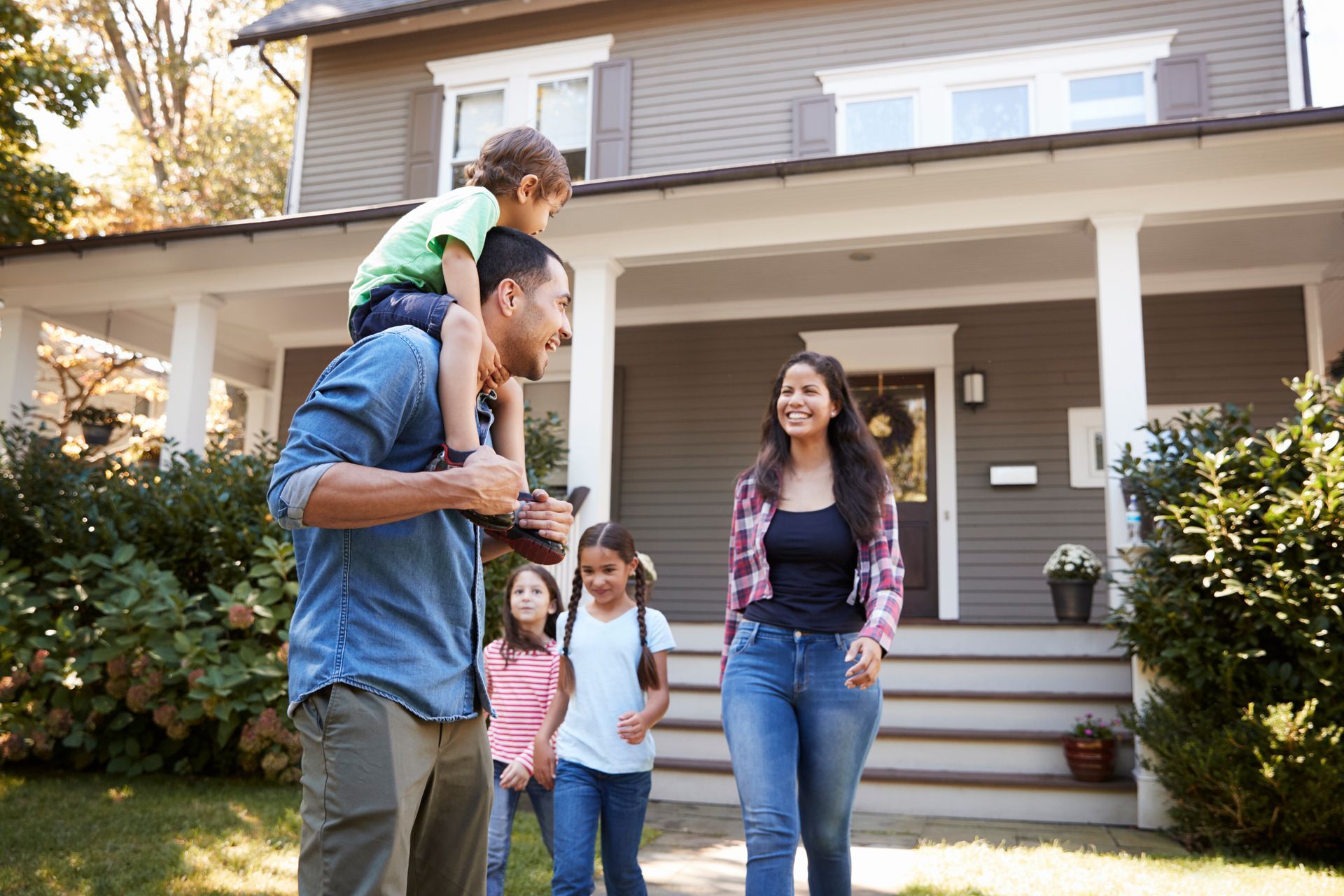 Family of five smiling, walking toward a house with a porch.