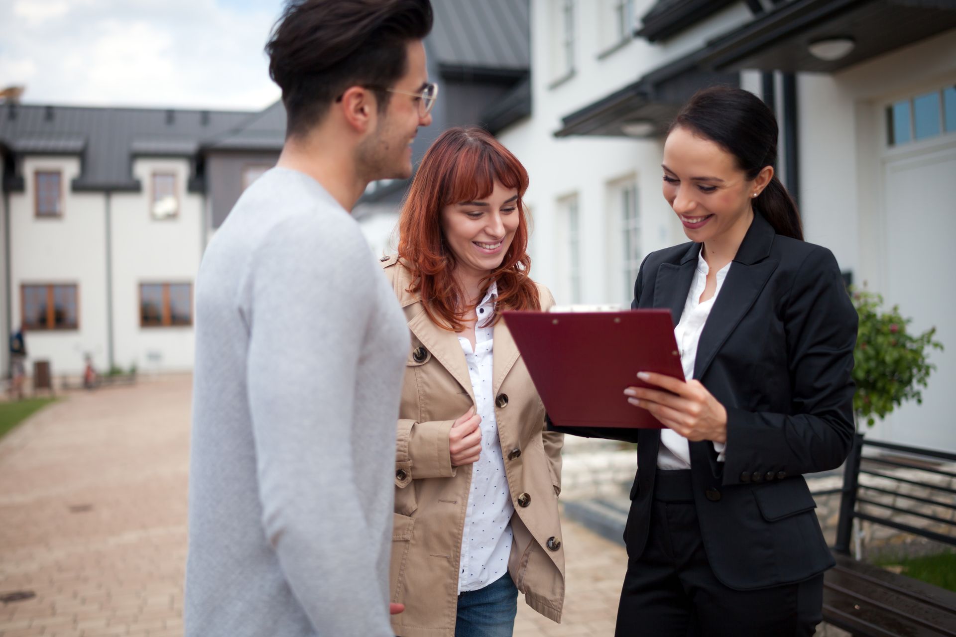Real estate agent showing paperwork to a couple outside a house. Real estate agent showing paperwork to a couple outside a house.