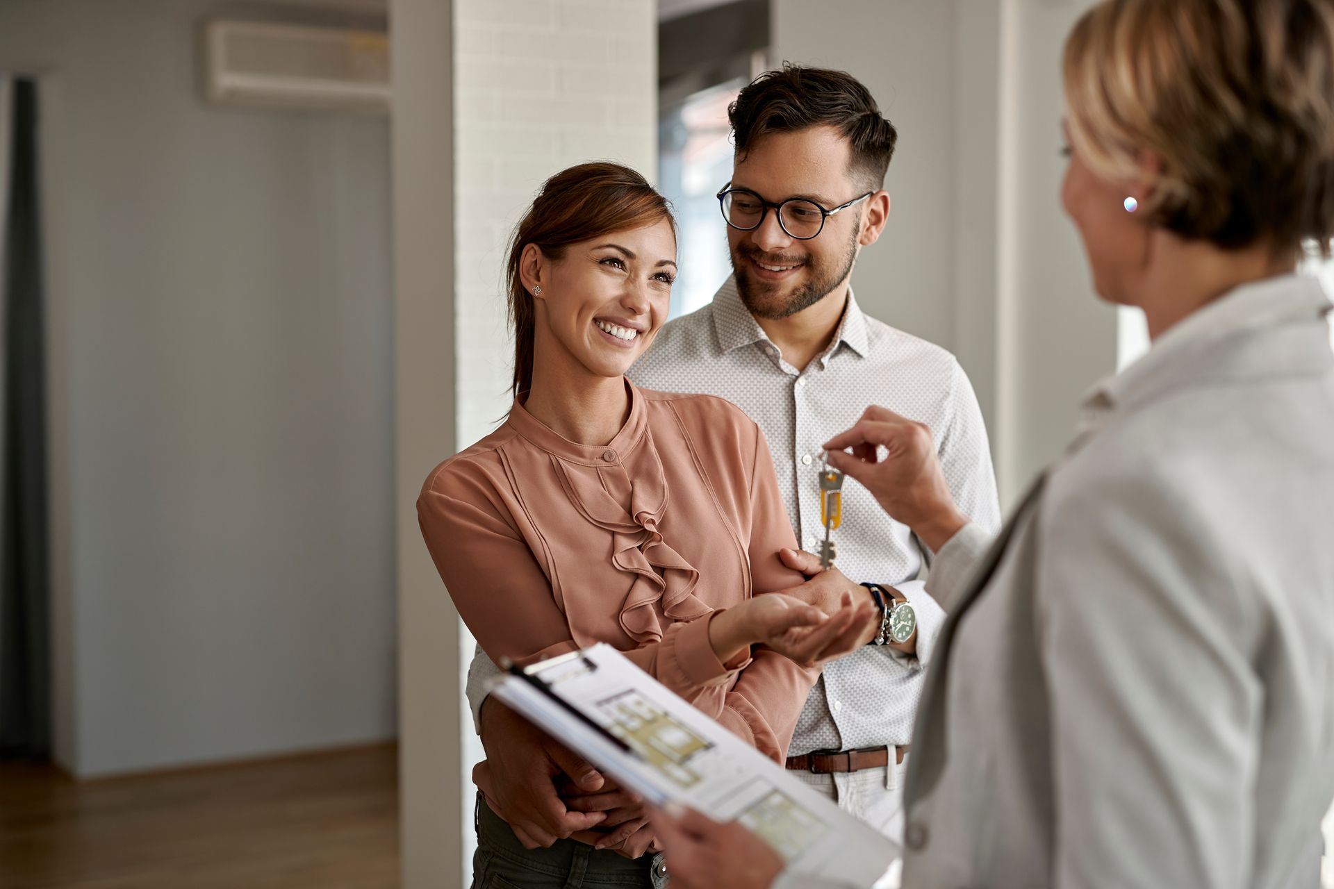 Couple receiving house keys from a real estate agent. They are smiling in a bright, modern interior. Couple receiving house keys from a real estate agent. They are smiling in a bright, modern interior.