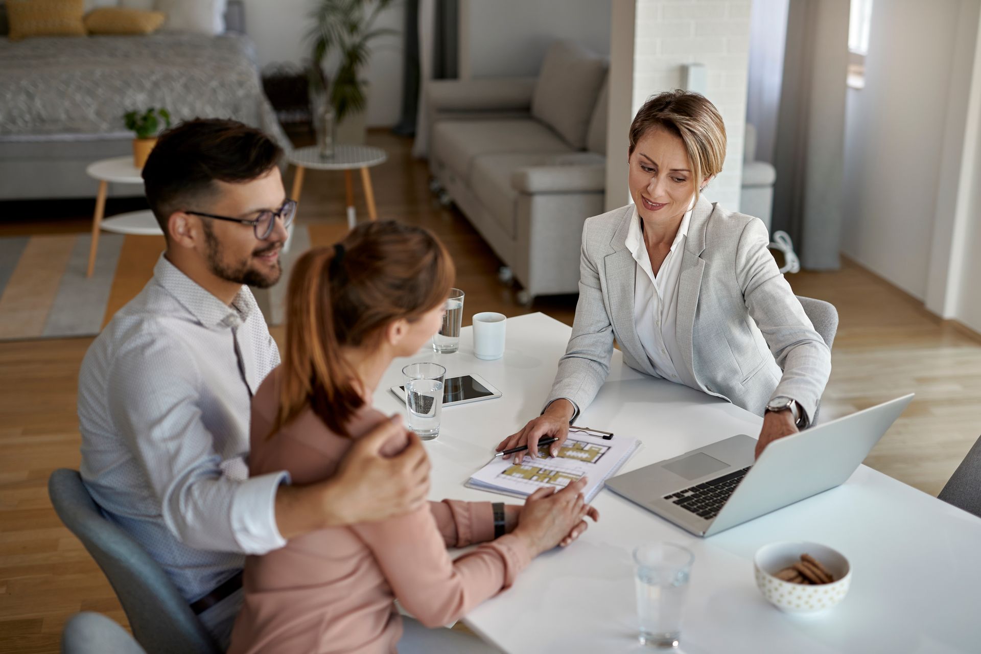 A real estate agent reviews documents with a couple at a table in a home. A real estate agent reviews documents with a couple at a table in a home.
