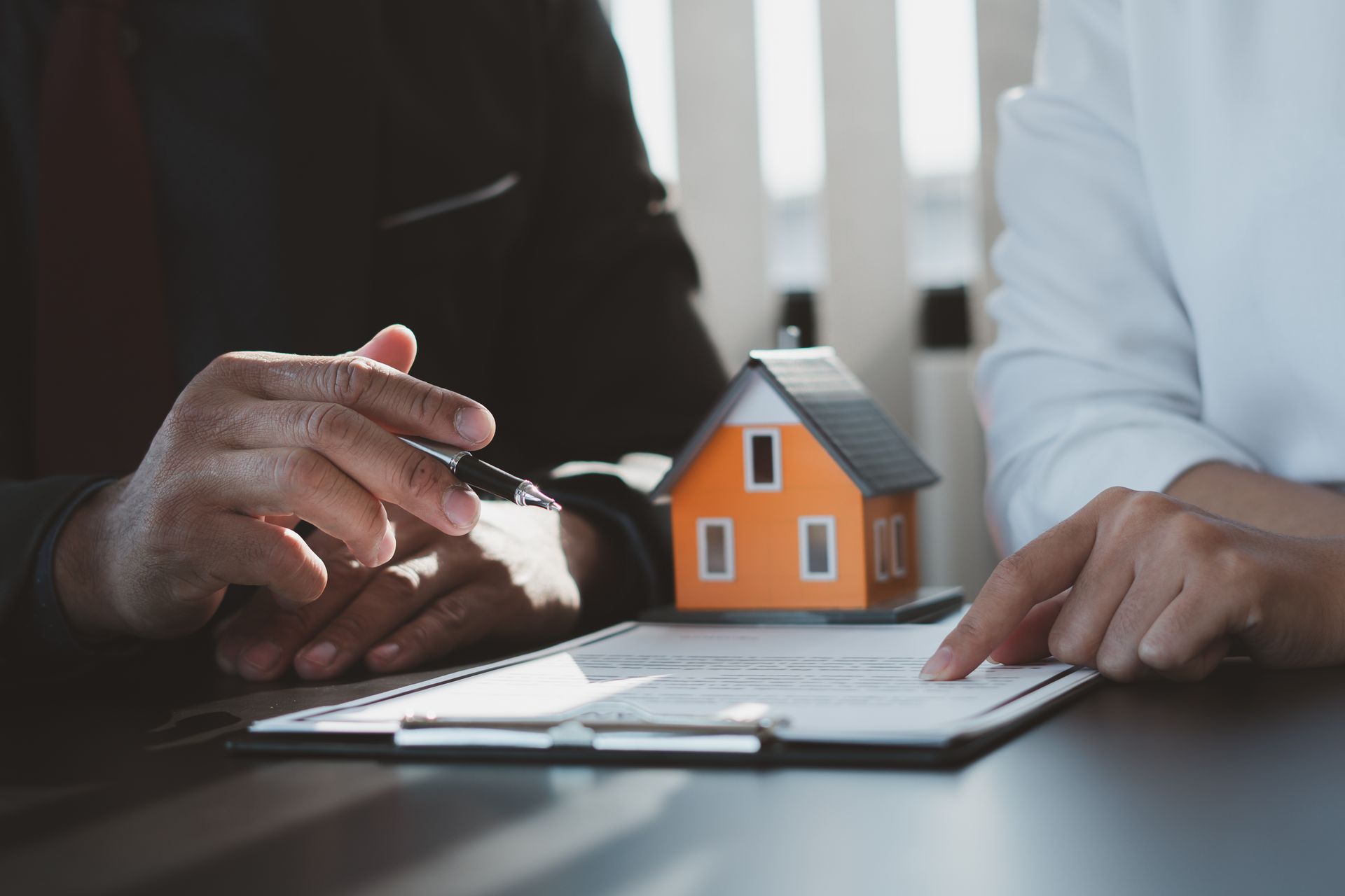 Hands pointing to a document with a miniature orange house.