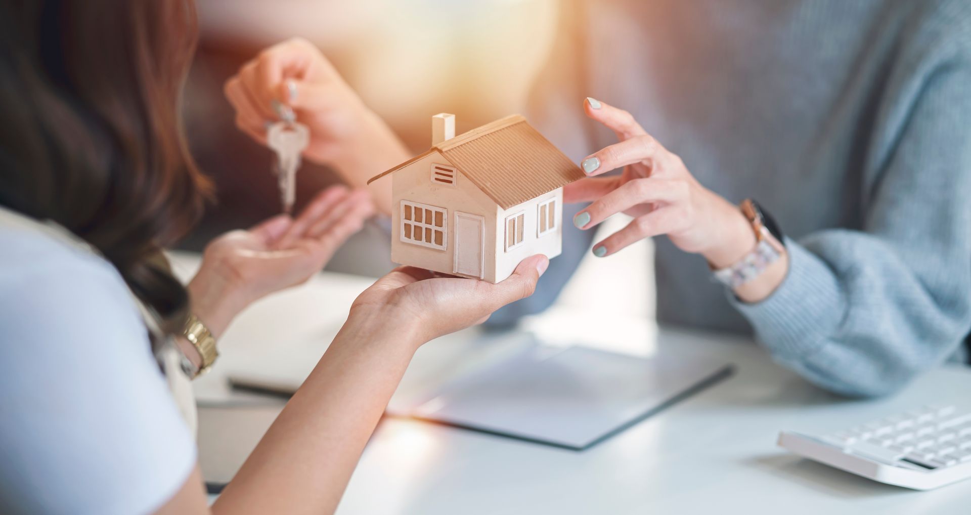 Two people exchanging keys and a miniature house model on a table.