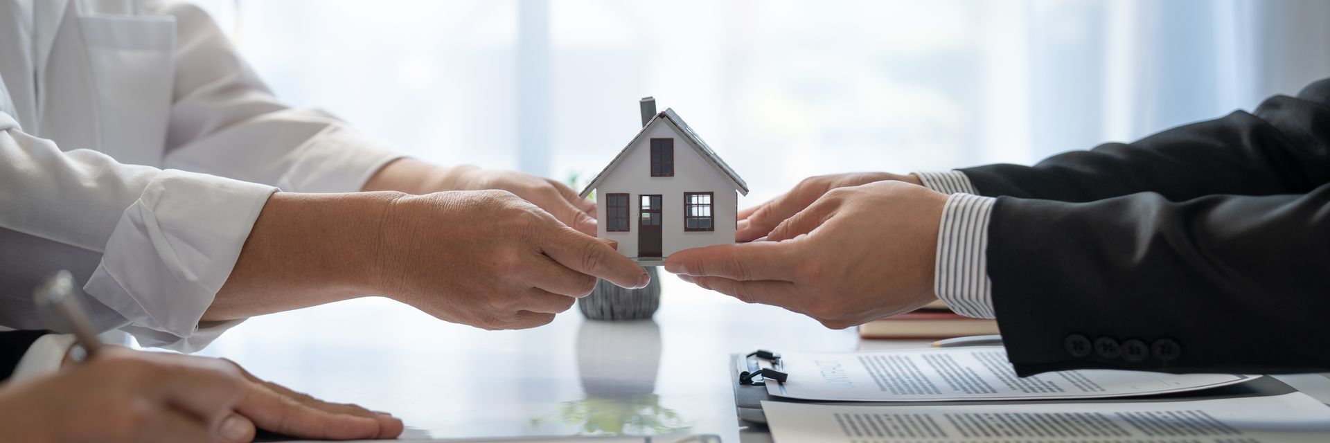 Hands passing a small house model over a table. A business deal or transaction.