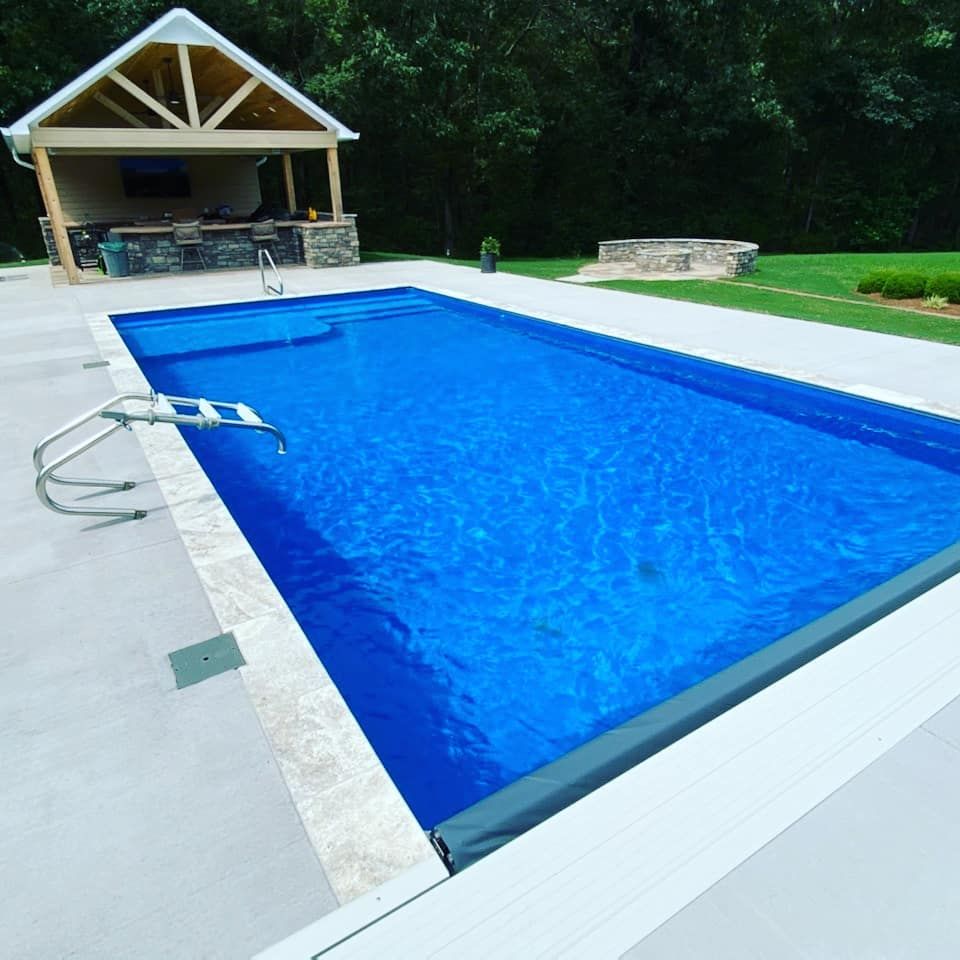 A rectangular swimming pool with blue water, a concrete deck, and a poolside pavilion.