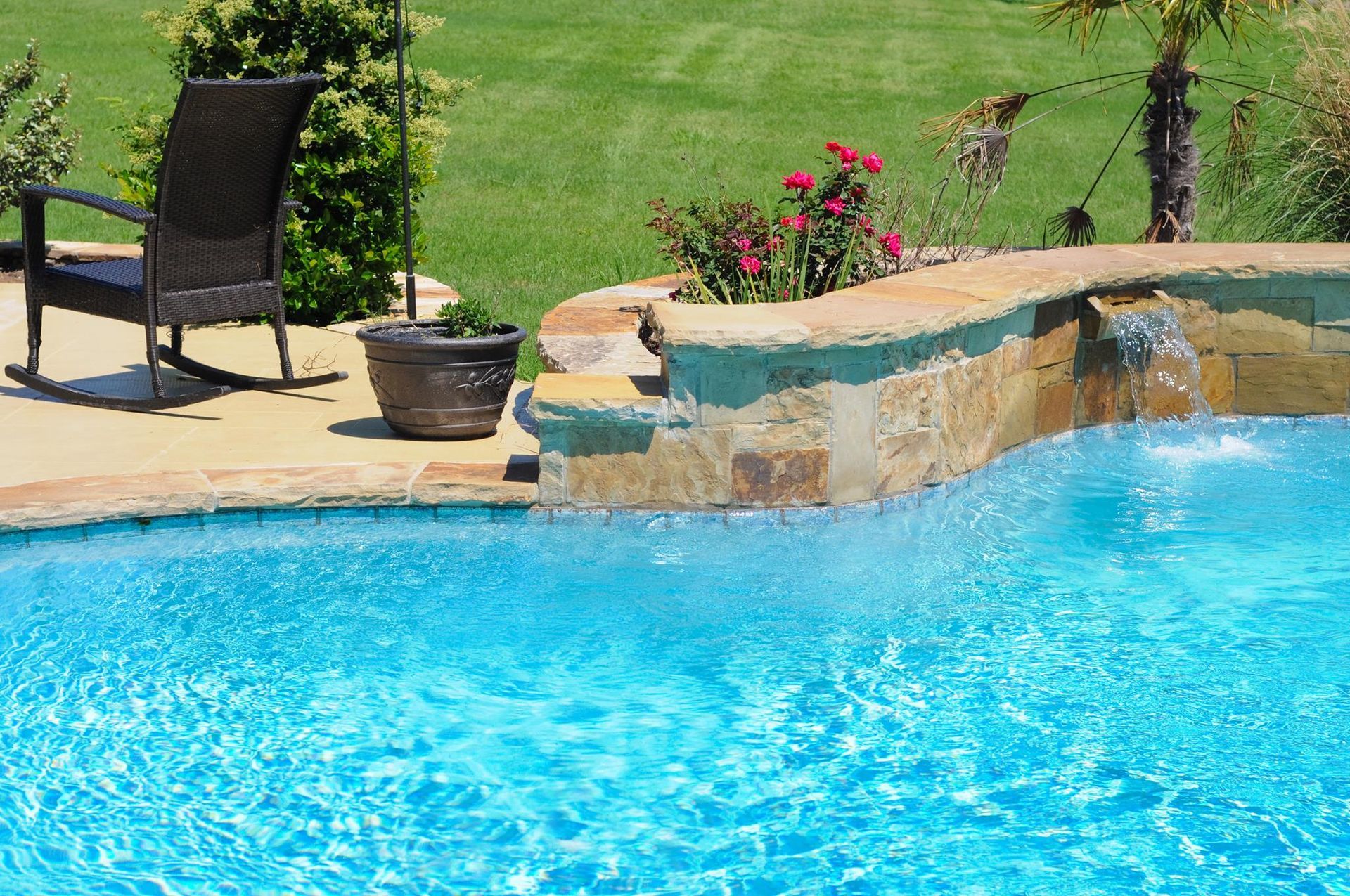 Swimming pool with blue water, stone waterfall, and a chair on the deck.