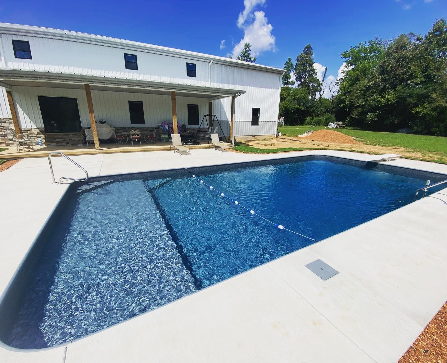 Rectangular pool in front of a white barn-like building on a sunny day.