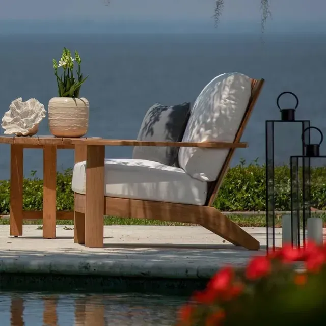 Wooden chair with white cushions, table with decor, overlooking water.
