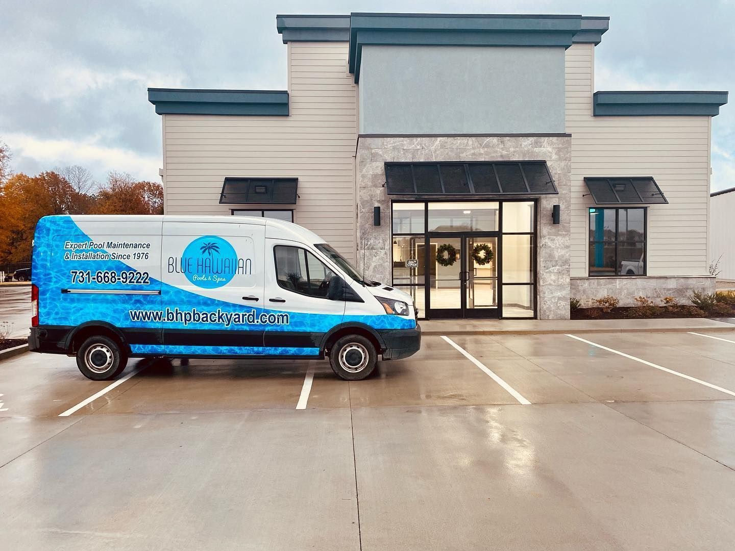 White service van with blue graphics parked in front of a business with glass doors and light gray stone facade.