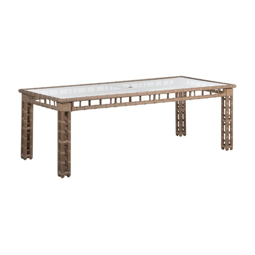 Rectangular outdoor dining table with glass top and woven brown frame.