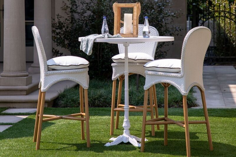 Outdoor white bistro set with high-backed chairs, cushions, and a small table set on a grassy lawn.
