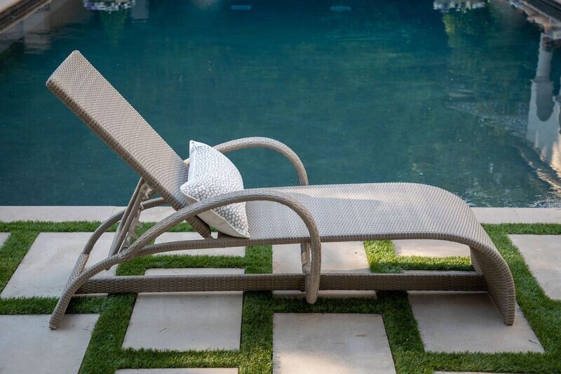 Wicker chaise lounge with a pillow beside a pool on a stone patio.