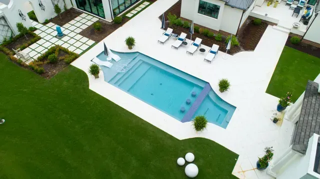 Aerial view of a luxury backyard with a pool, lounge chairs, and lush green grass. White and turquoise color scheme.