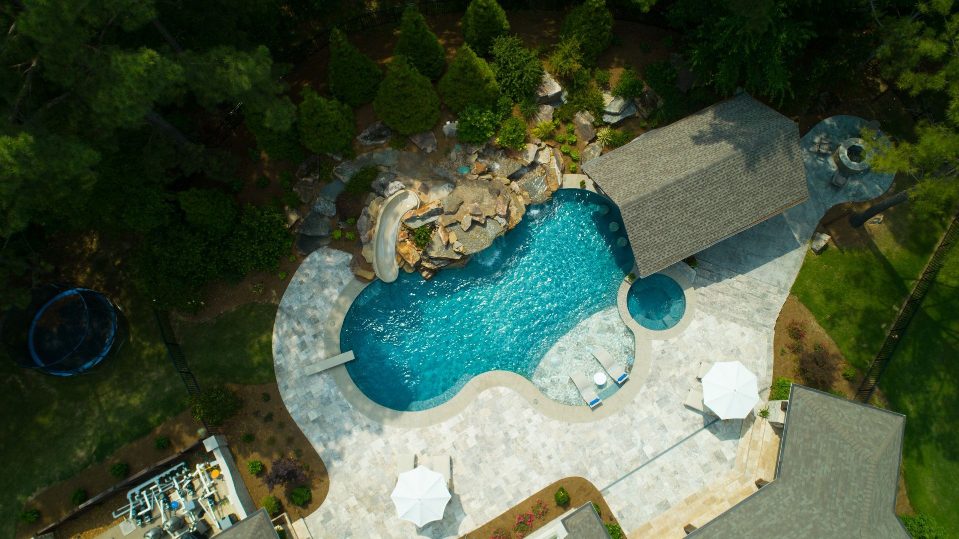 Aerial view of a luxurious backyard pool with a waterfall, gazebo, and surrounding landscaping.