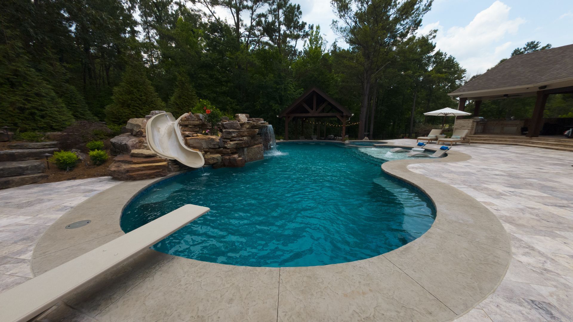 Swimming pool with a slide, diving board, and waterfall feature in a backyard setting.
