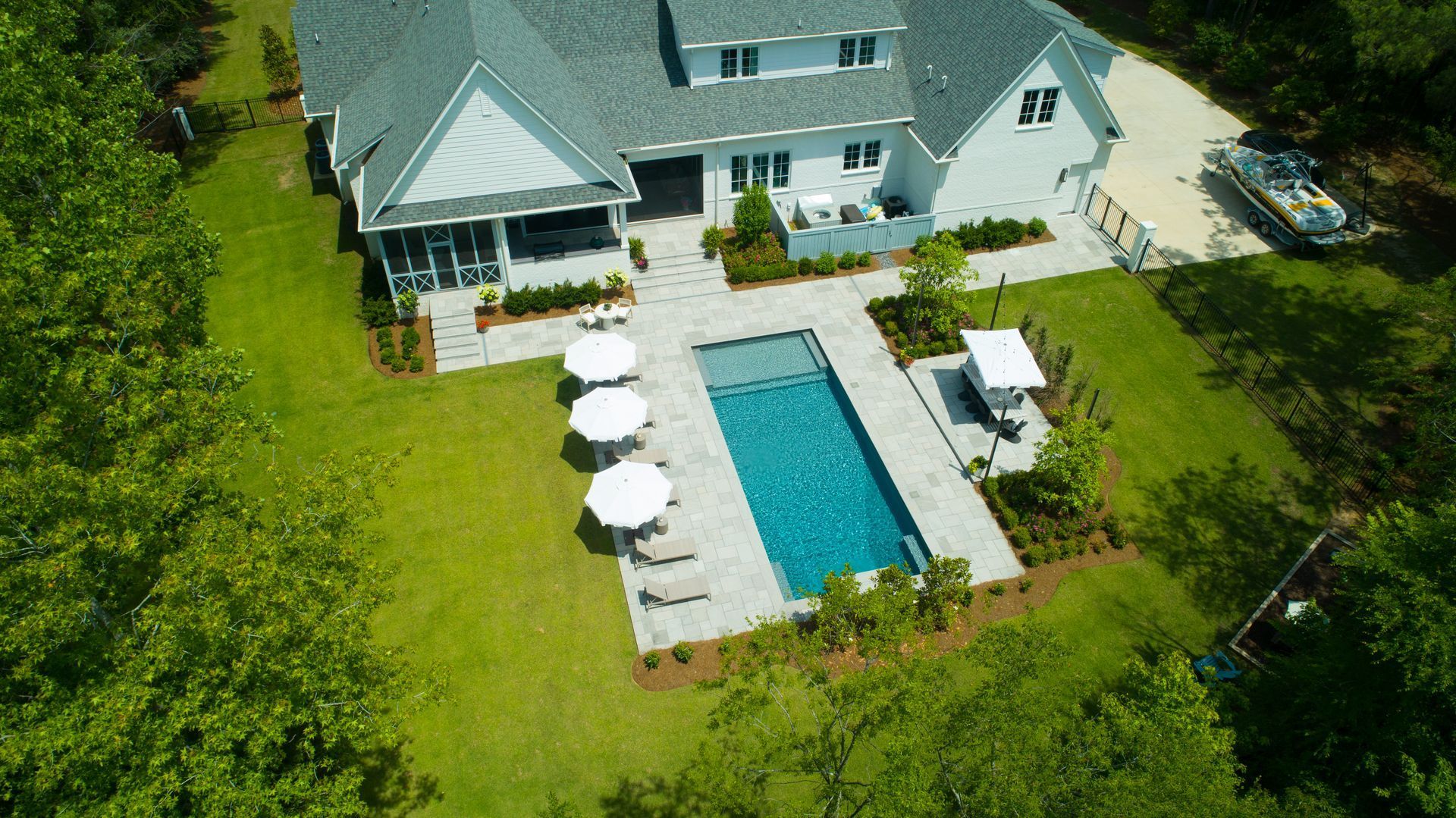 Aerial view of a house with a pool, patio, and umbrellas on a grassy lawn.