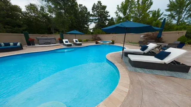 Swimming pool with lounge chairs, umbrellas, and spa in a backyard setting.