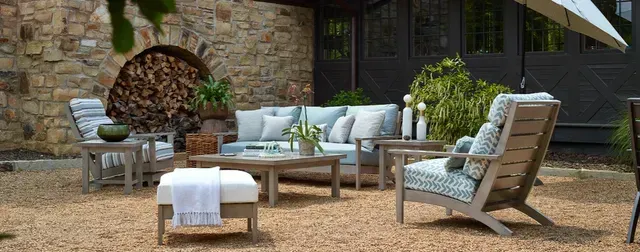 Outdoor patio furniture set on a gravel surface with a stone wall backdrop.