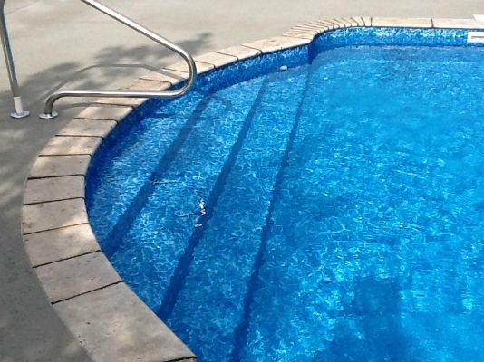 Pool with blue water, curved steps, and a stainless steel handrail.