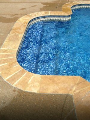 Swimming pool with blue water and beige stone coping.