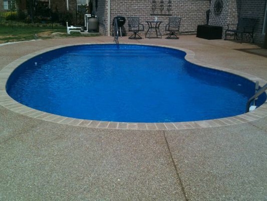 Blue swimming pool surrounded by a tan concrete patio.