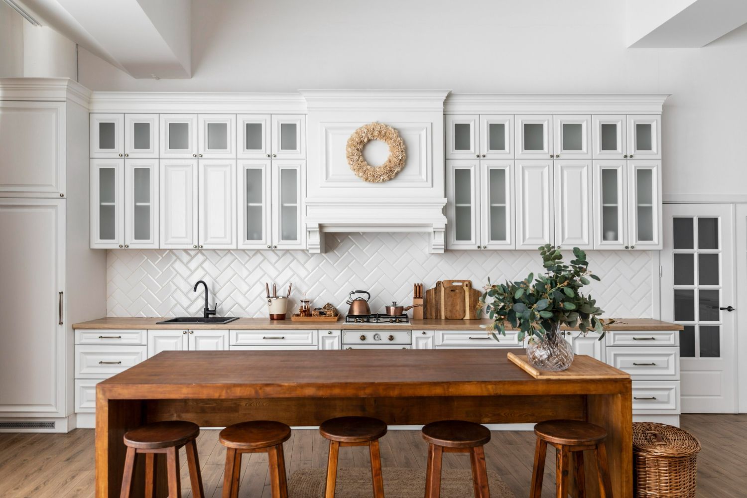 A kitchen with white cabinets , a wooden table and stools.