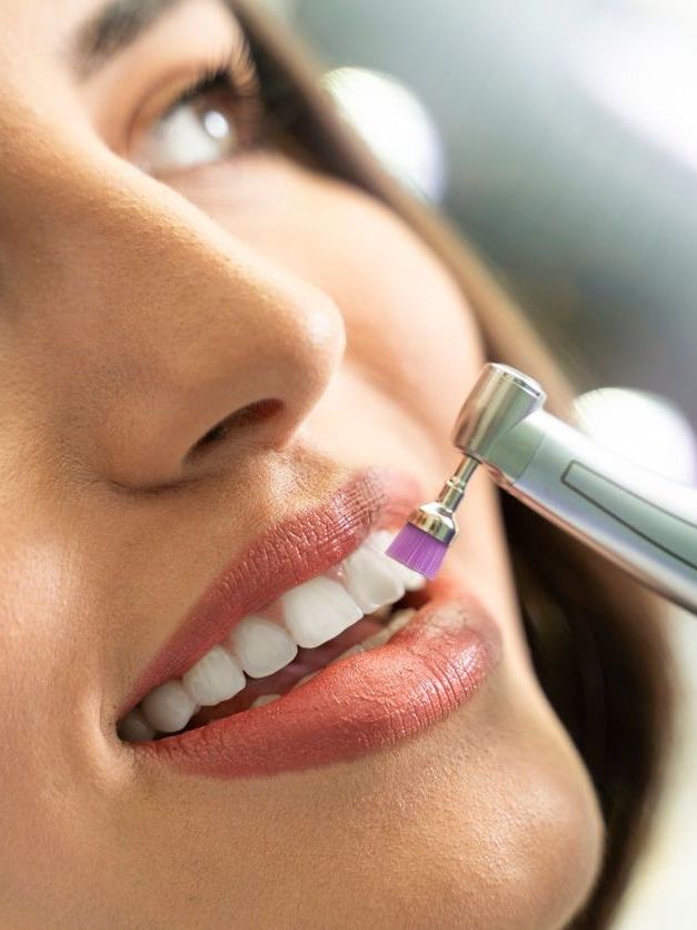 A woman is getting her teeth polished by a dentist.