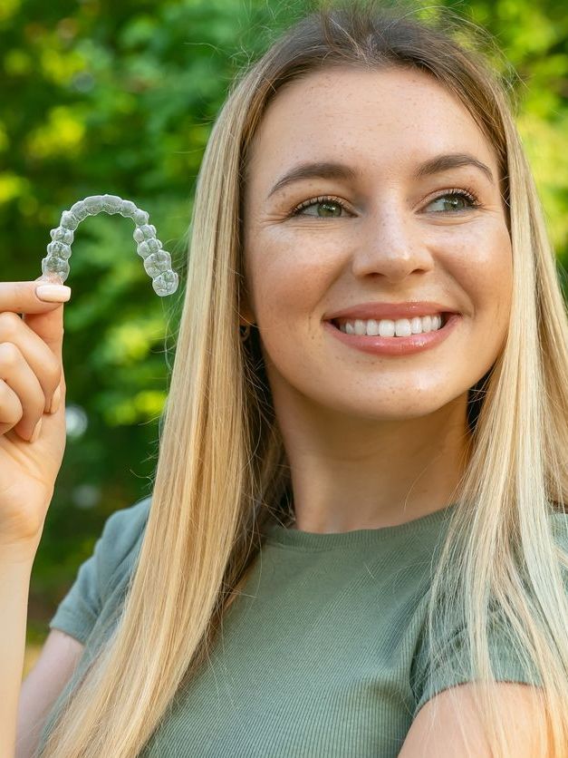 A woman is smiling while holding a clear brace in her hand.