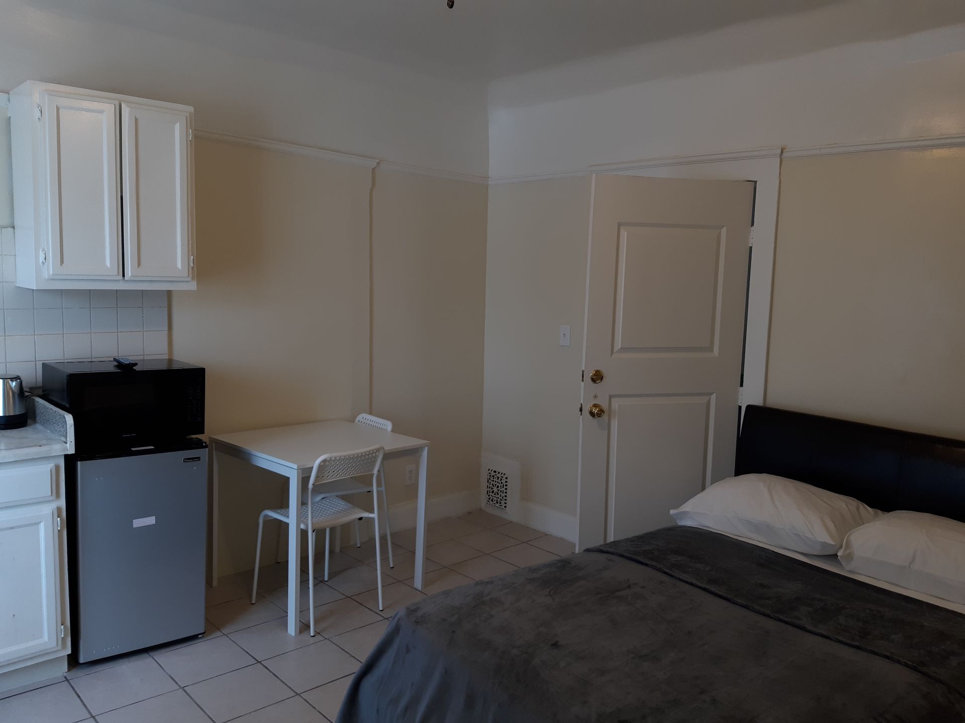 A bedroom with a bed , table , chairs and a refrigerator.
