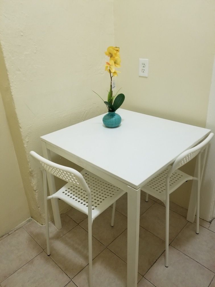 A white table with two chairs and a vase of flowers on it