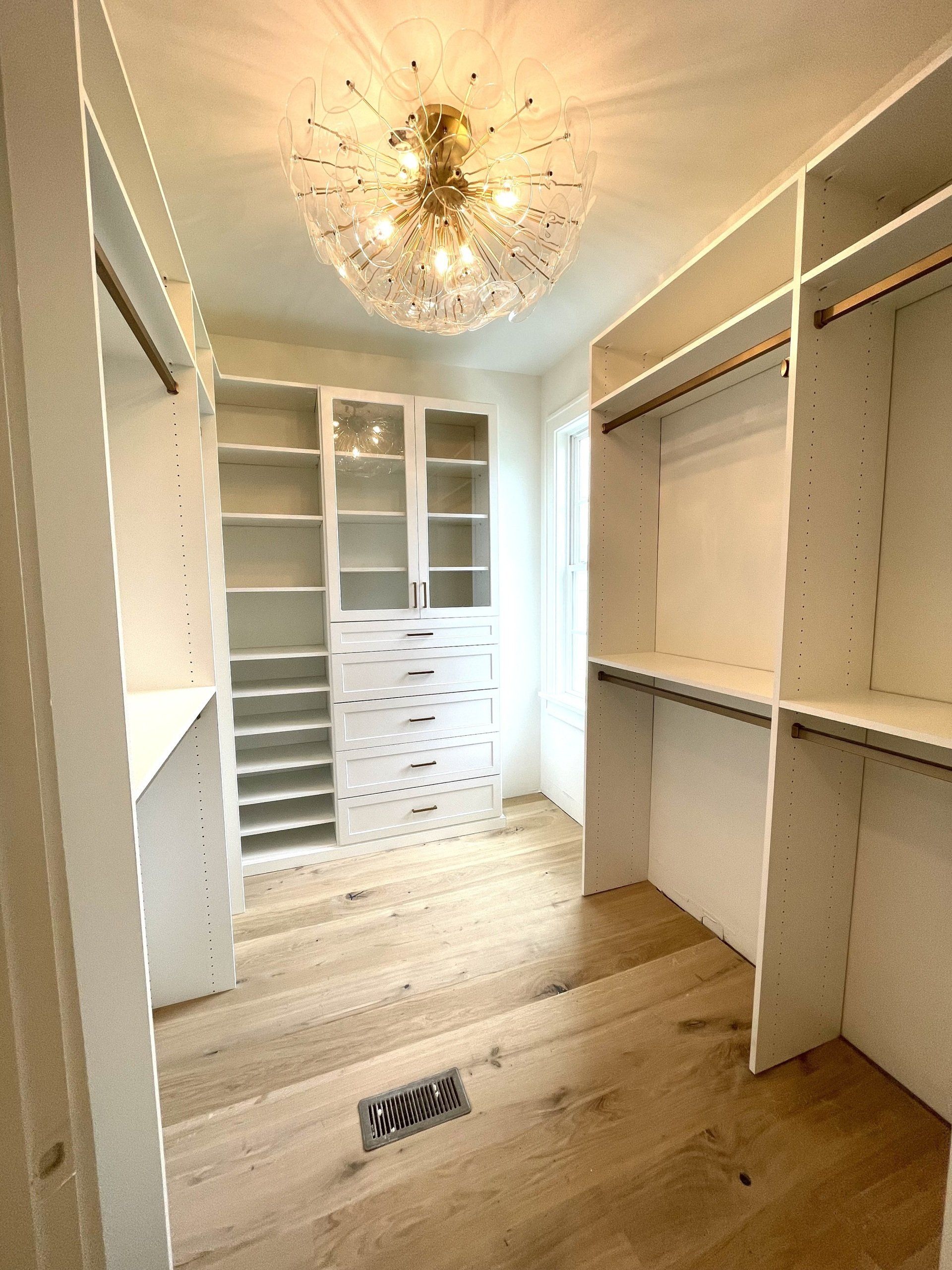 A walk in closet with lots of shelves and a chandelier.