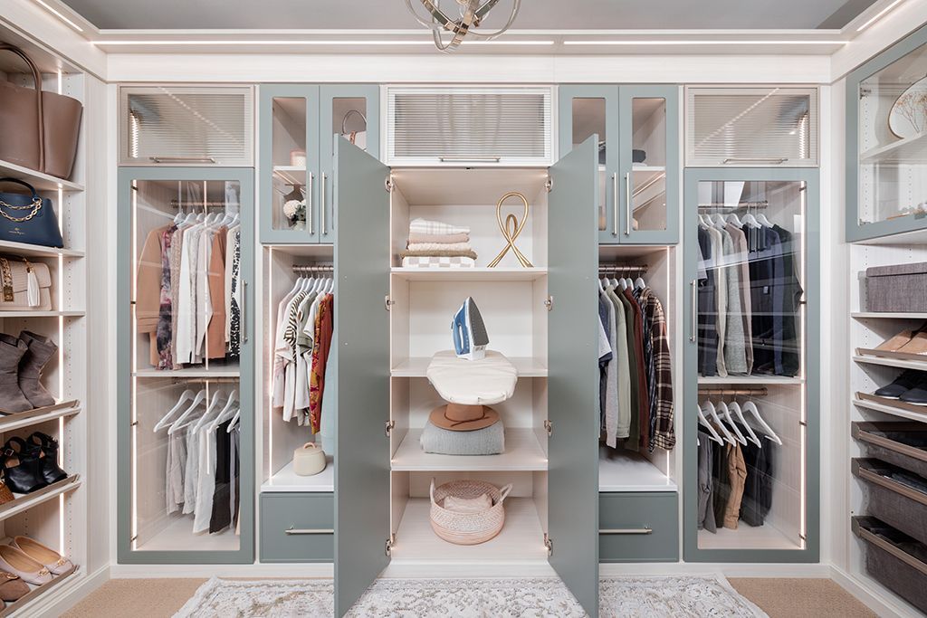 Elegant walk-in closet with built-in shelves, hanging clothes, and a central vanity chair in soft neutral tones