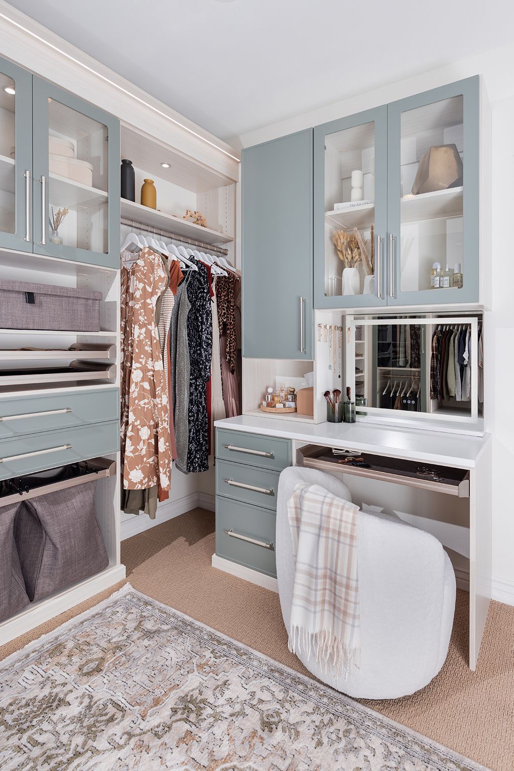 Bright walk-in closet with white vanity, gray cabinets, hanging clothes, mirror, and patterned rug