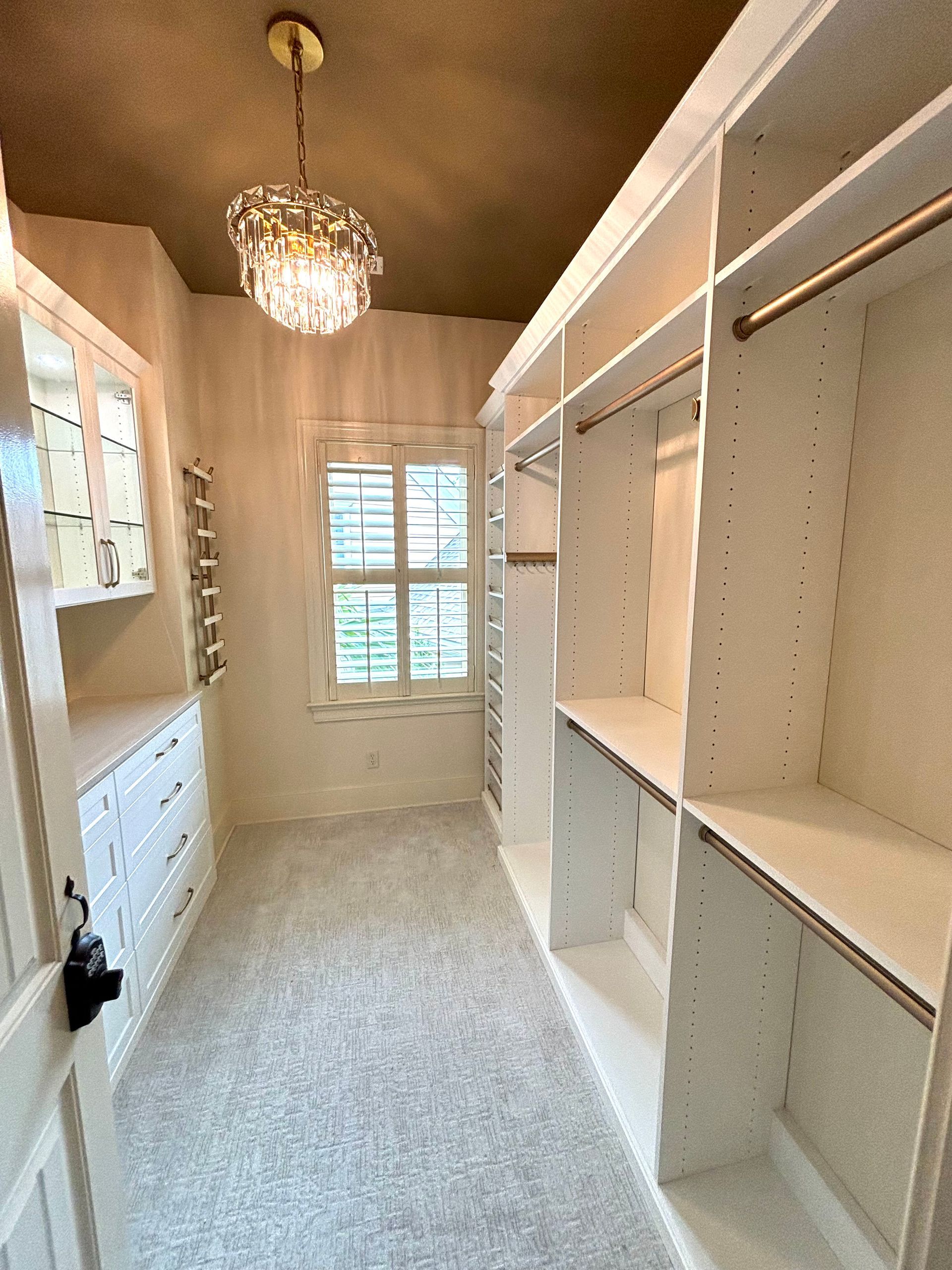 A walk in closet with lots of shelves and a chandelier hanging from the ceiling.