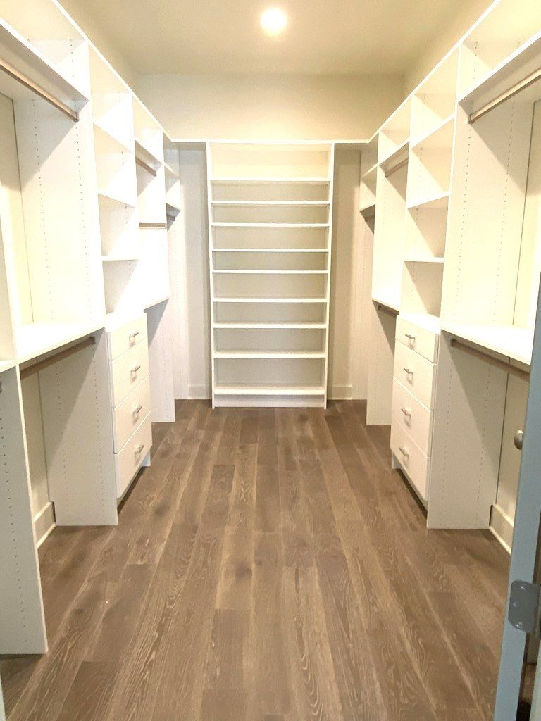 A walk in closet with hardwood floors and white shelves.