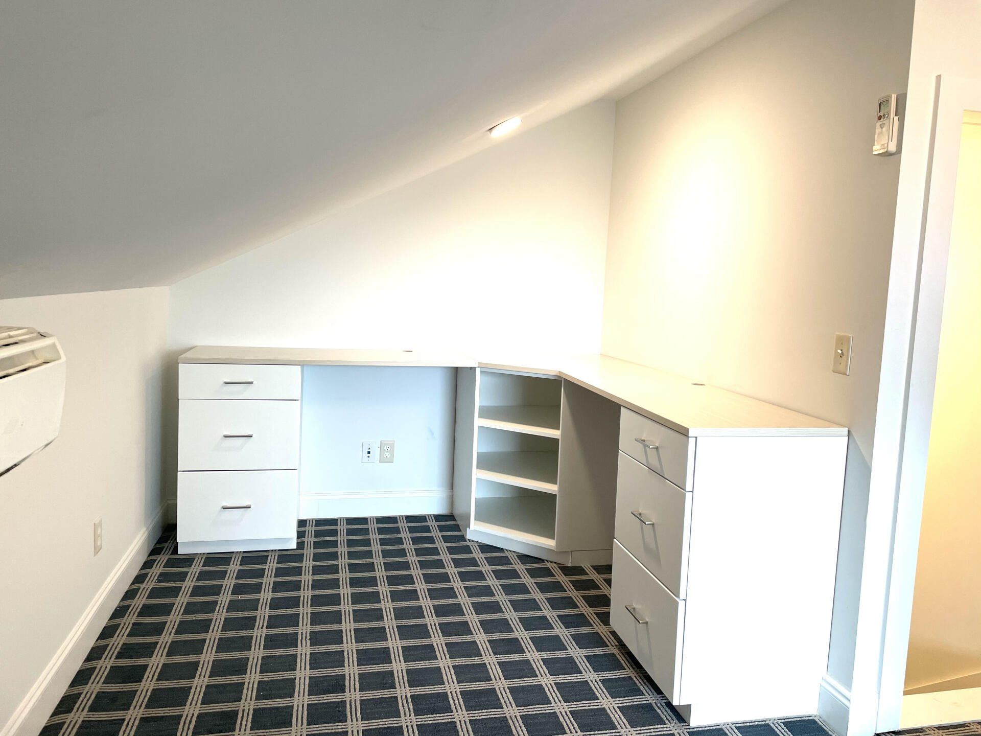 A corner of a room with a desk and drawers