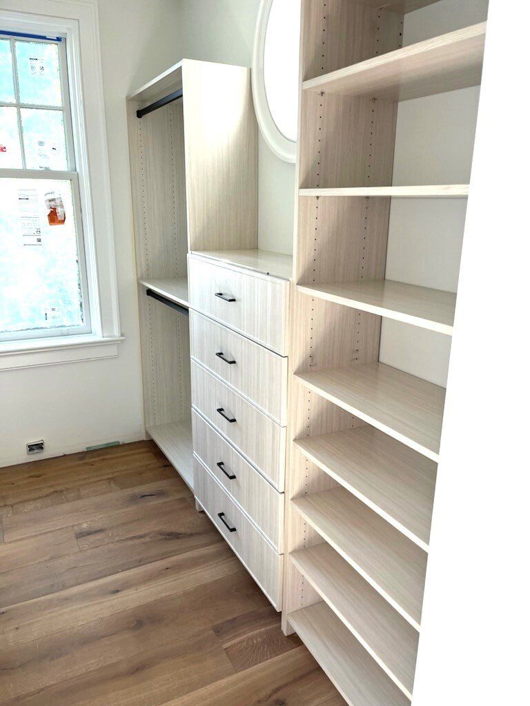A walk in closet with lots of shelves and drawers and a window.