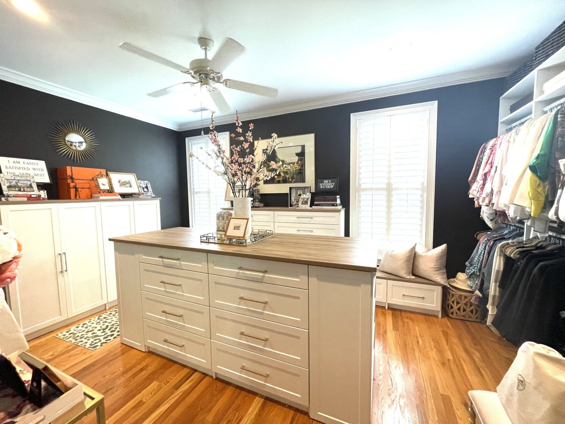 A walk in closet with a large island in the middle and a ceiling fan.