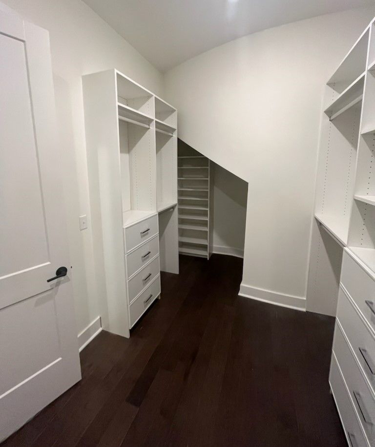 A walk in closet with lots of shelves and drawers under a staircase.