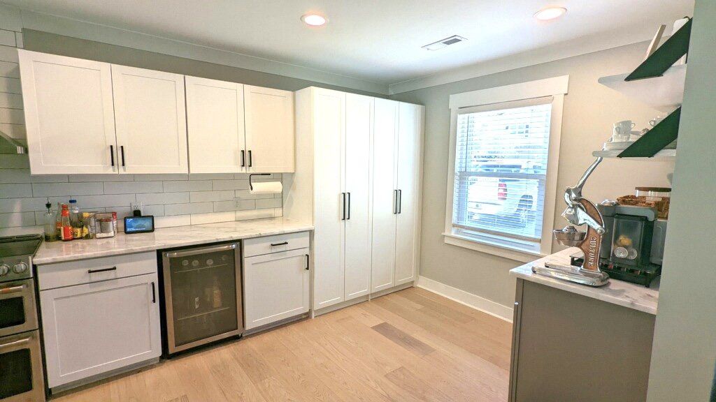 A kitchen with white cabinets , stainless steel appliances , a refrigerator and a window.
