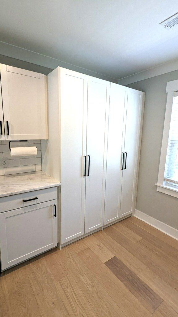 A laundry room with white cabinets , a dishwasher , and a window.
