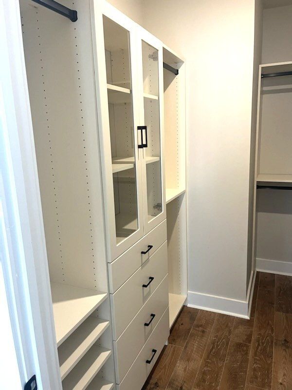 A walk in closet with white shelves , drawers , and glass doors.