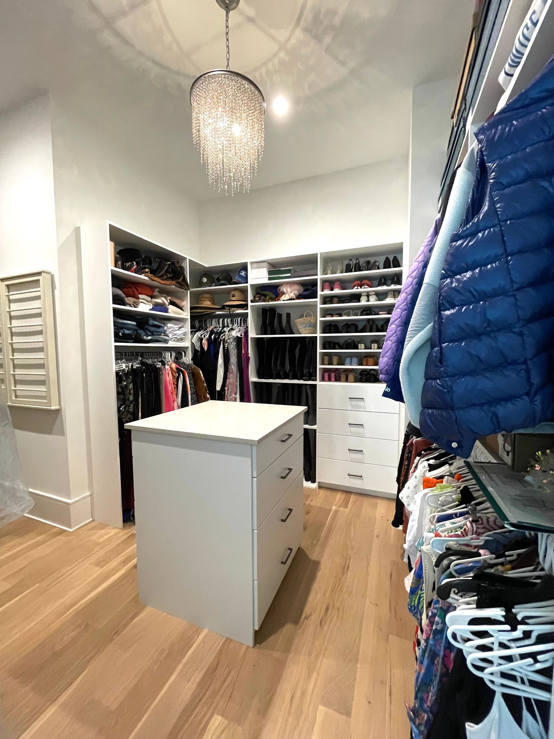 A walk in closet with lots of clothes and a large island in the middle.
