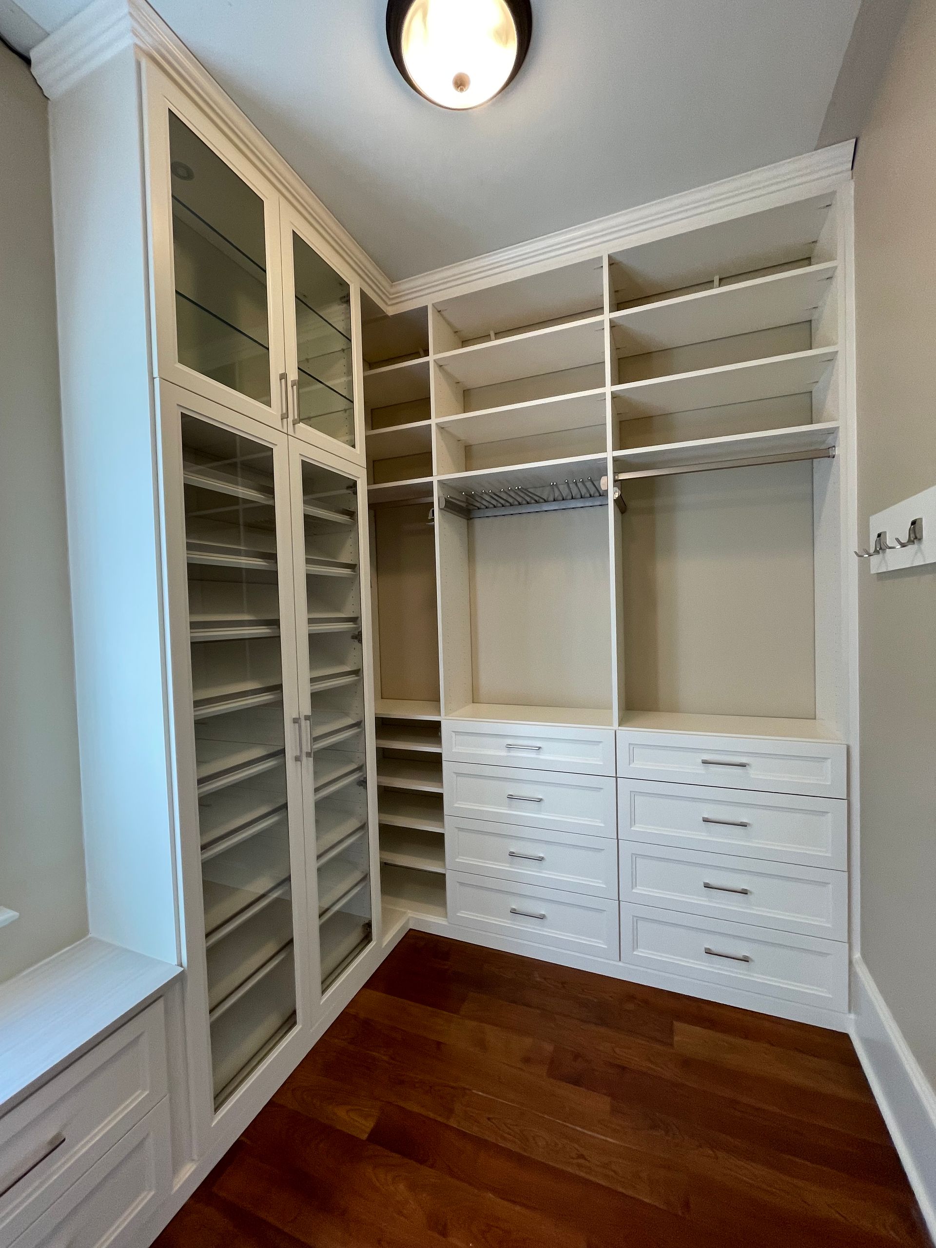 A walk in closet with white cabinets and glass doors.