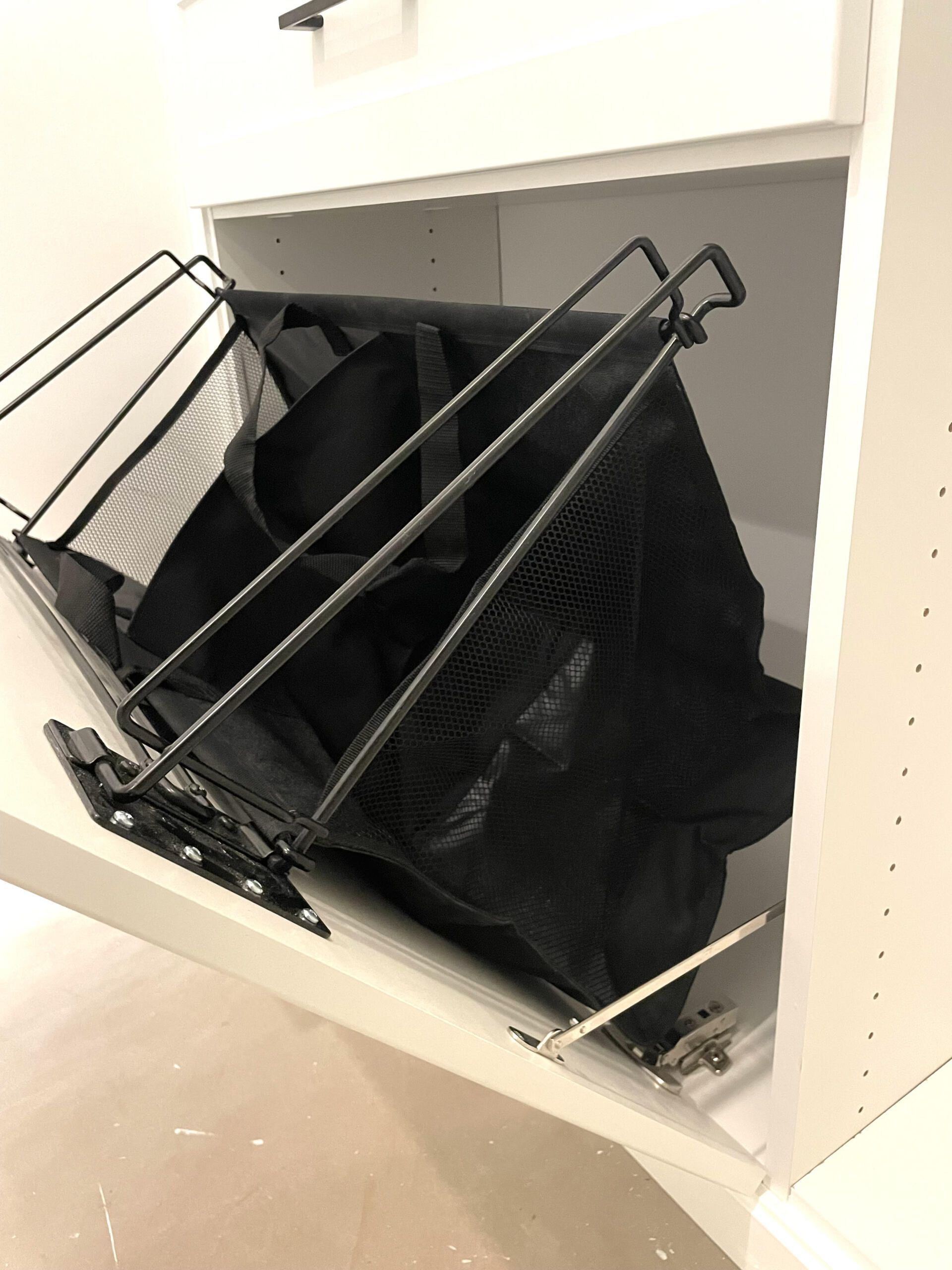A black laundry basket is sitting inside of a white cabinet.